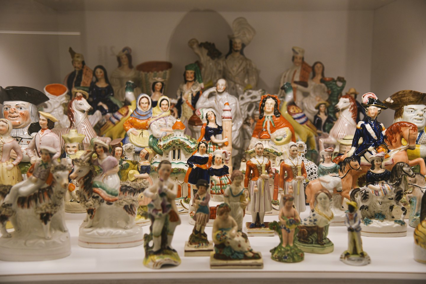 Antyczne ceramiczne figurki ustawione razem na białej półce.